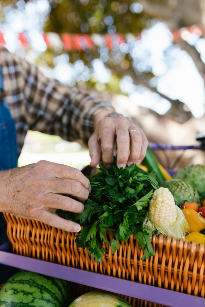 Hands arranging fresh vegetables in a basket at an outdoor farmers market.
